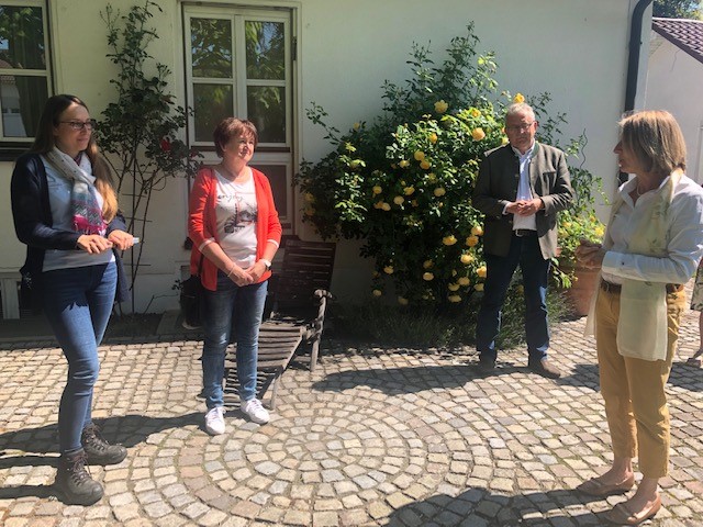 Simone Schmitt (Kreisfachberatung), Monika Edenhofer (Kreisvorsitzende Obst- und Gartenbauvereine), Landrat Josef Laumer (von links) zu Besuch im Garten von Margit Kastl (rechts) in Leiblfing auf der Terrasse vor einem Rosenstrauch.