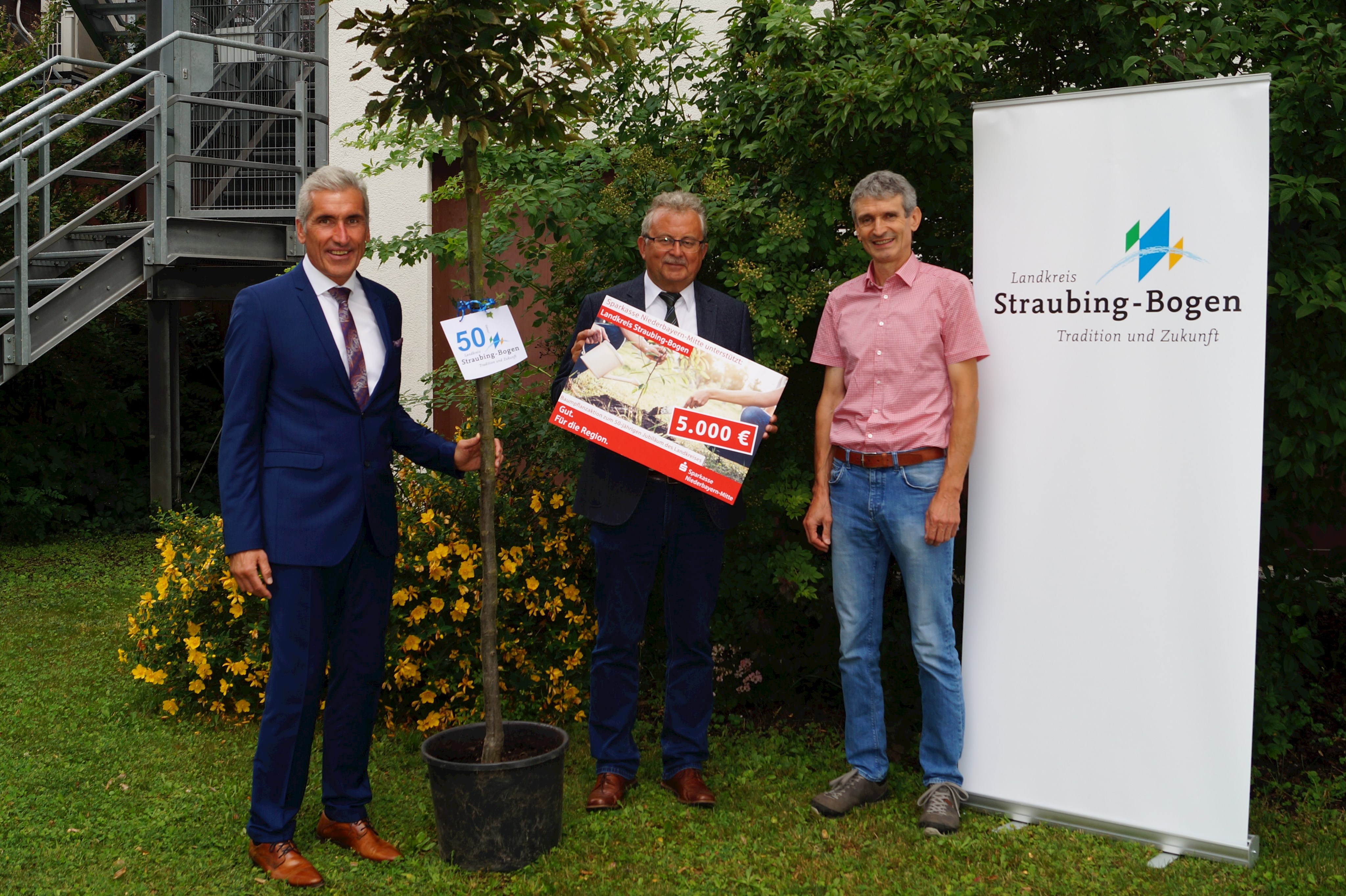 Walter Strohmaier (Vorstandsvorsitzender der Sparkasse Niederbayern-Mitte), Landrat Josef Laumer und Harald Götz (Kreisfachberater des Landkreises Straubing-Bogen, von links) mit einem der Bäume der Pflanzaktion vor dem Landratsamt.