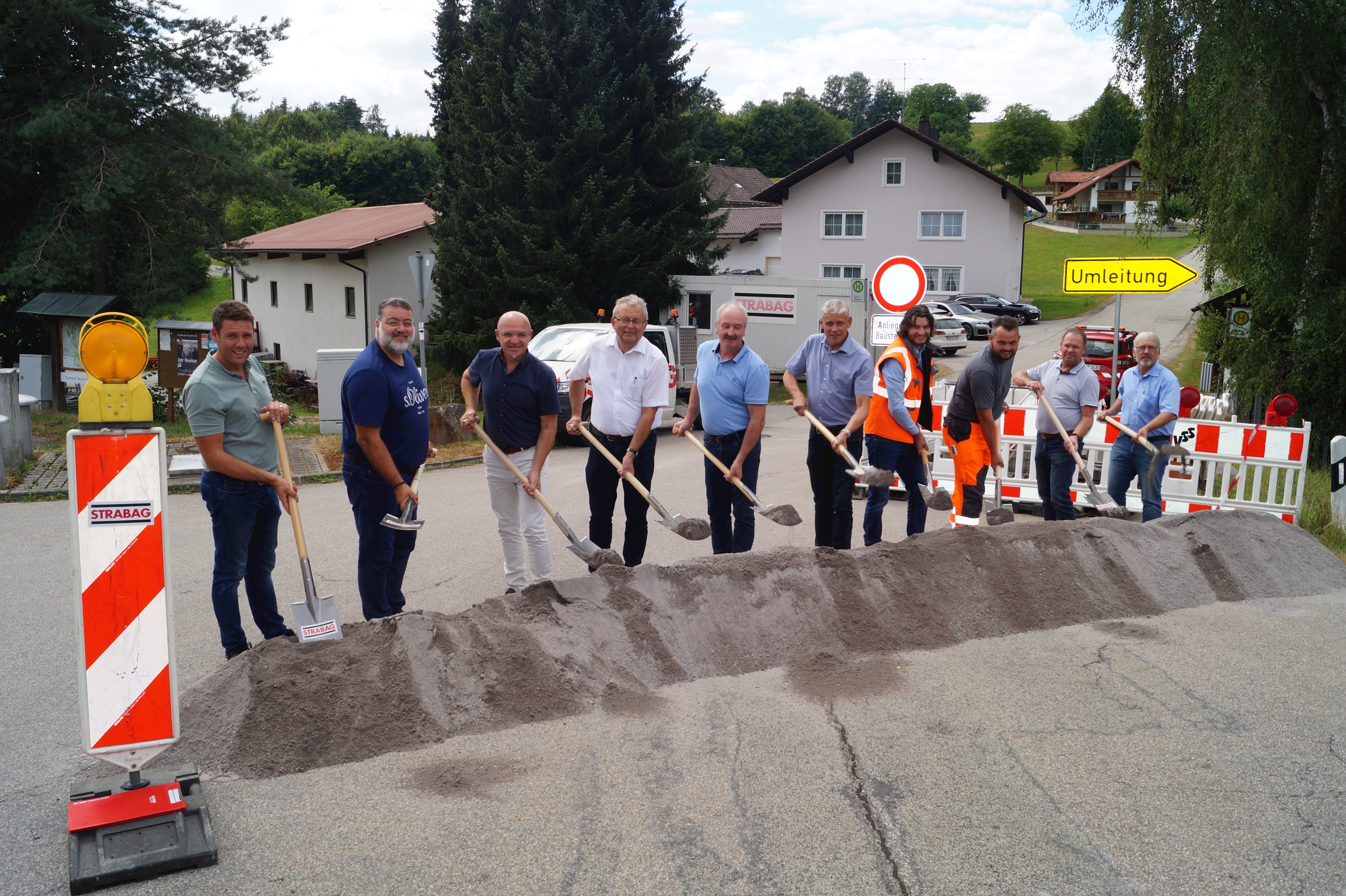 Beim Spatenstich stehen Landrat Josef Laumer (Vierter von links), Windbergs Bürgermeister Helmut Haimerl (Fünfter von links) und Perasdorfs Bürgermeister Thomas Schuster (ganz rechts), sowie Vertreter der Tiefbauverwaltung und der Firma STRABAG an der Kreisstraße SR 49.