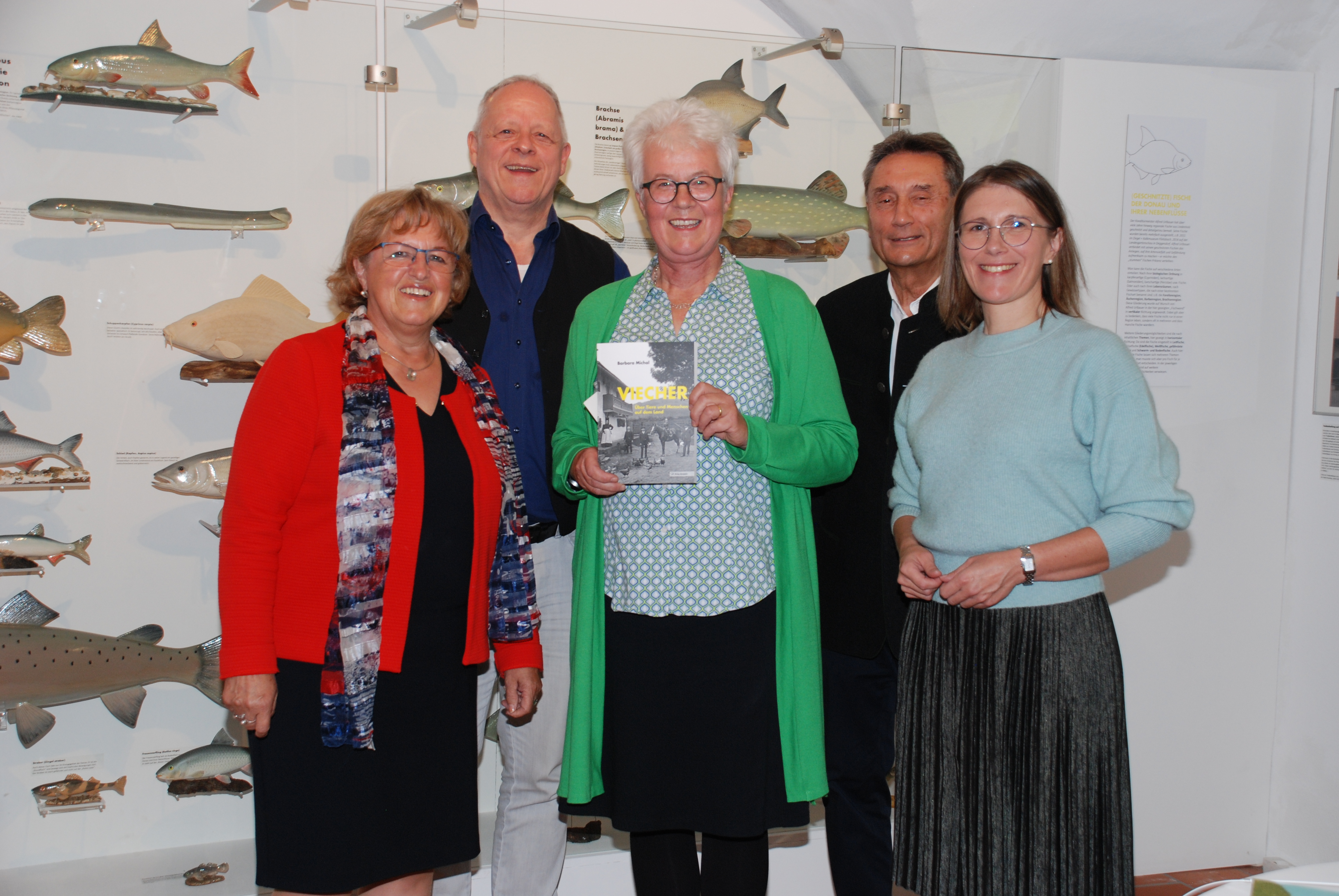Barbara Michal steht mit den Ehrengästen vor der Sonderausstellung und präsentiert das Buch zur Ausstellung.
