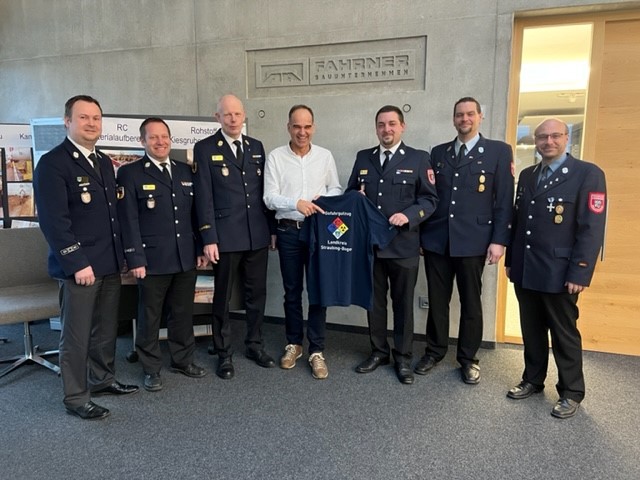 KBM Gefahrgut Albert Uttendorfer jun. (Dritter von rechts) übernimmt stellvertretend die Poloshirts von Firmeninhaber Robert Fahrner (mitte). Dabei stehen sie vor dem Eingang der Firma Fahrner.