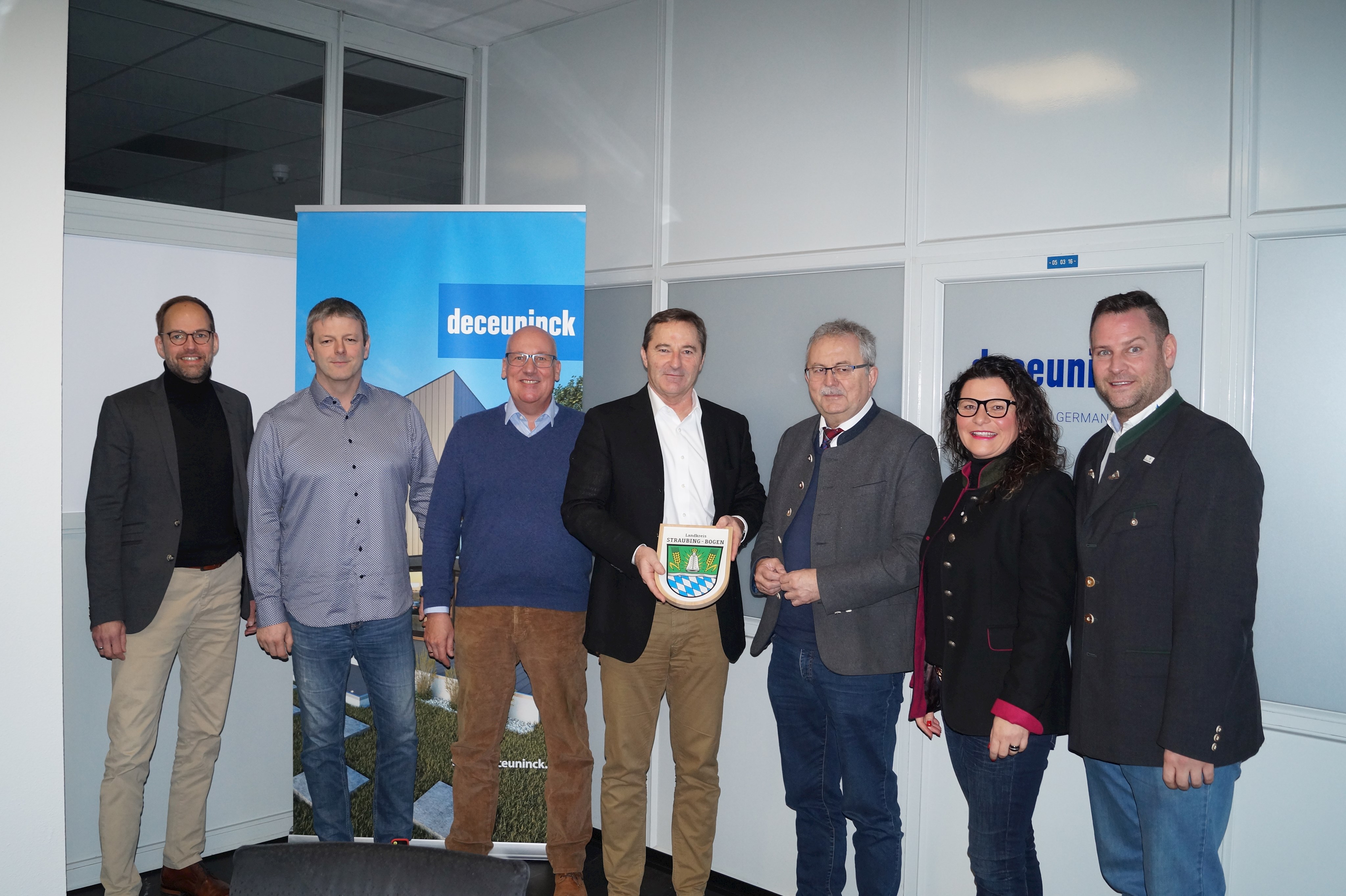 Jörn Schütte (Vertriebsleiter), Markus Kiefl (Betriebsratsvorsitzender), Patrick Hartmann (Personalleiter), Jörg Hofmann (neuer Geschäftsführer), Landrat Josef Laumer, Astrid Stierstorfer (Assistentin der Geschäftsleitung) und Wirtschaftsreferent Martin Köck (von links) stehen im Besprechungszimmer von Deceuninck und Landrat Laumer überreicht ein Erinnerungsgeschenk.