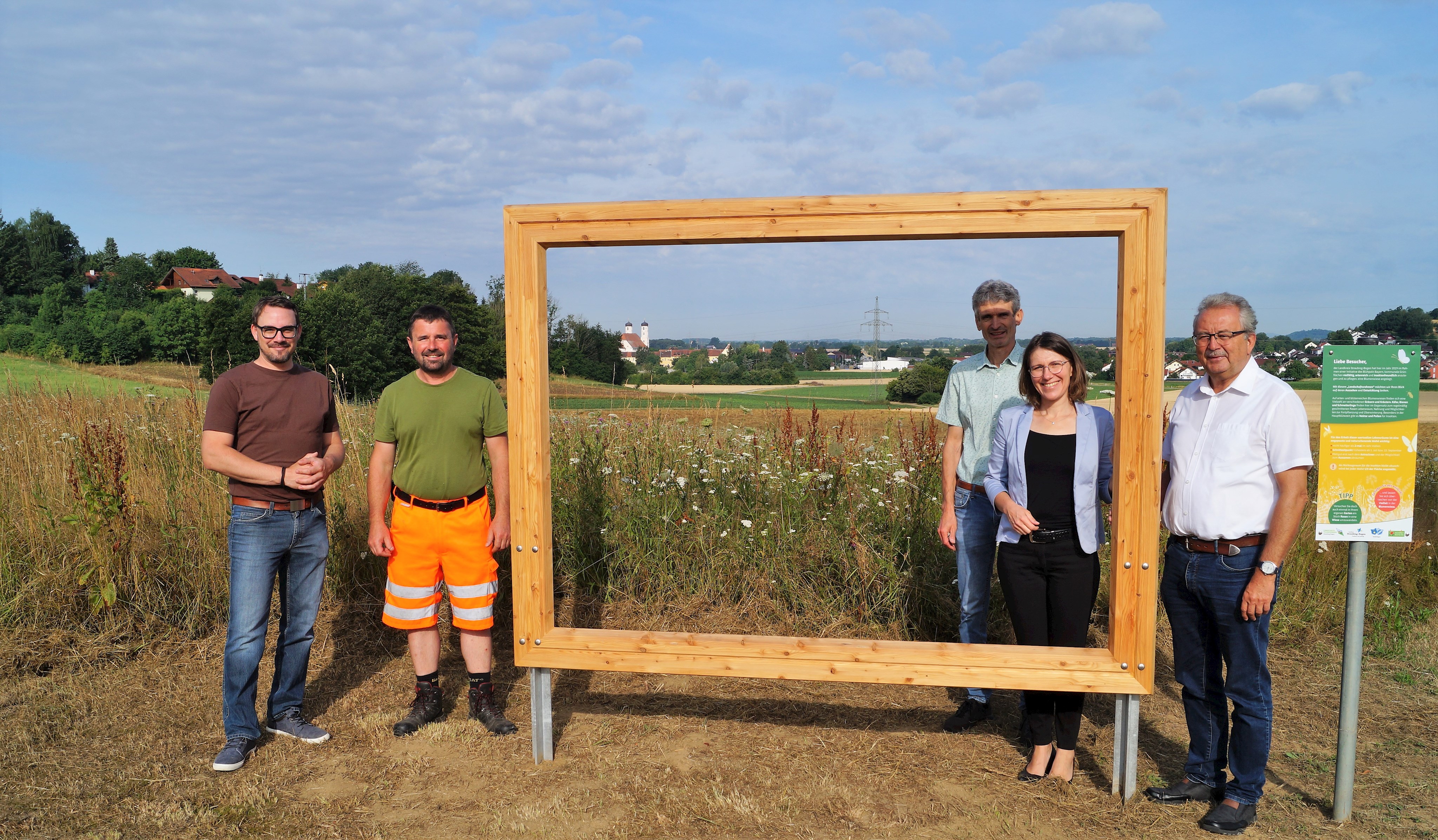 Ambros Köppl (Landschaftspflegeverband), Hubert Kienberger (Kreisbauhof Ittling), Kreisfachberater Harald Götz, Bogens Bürgermeisterin Andrea Probst und Landrat Josef Laumer (von links) stehen am Landschaftsrahmen neben dem Schulzentrum in Bogen. Im Hintergrund die Blühwiese und links die Klosterkirche in Oberalteich.