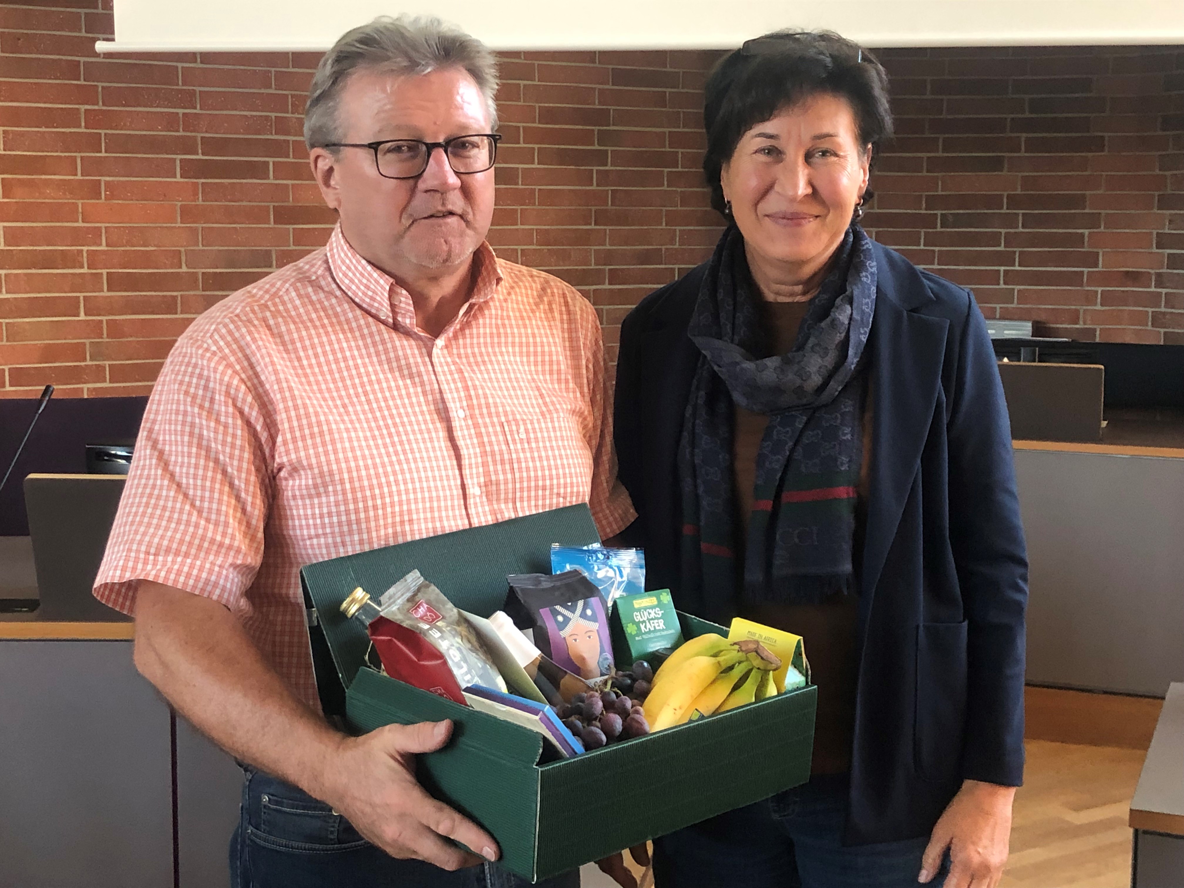 Anita Karl übergibt Klaus Achatz nach seiner letzten Steuerungsgruppen-Sitzung einen Geschenkkorb.