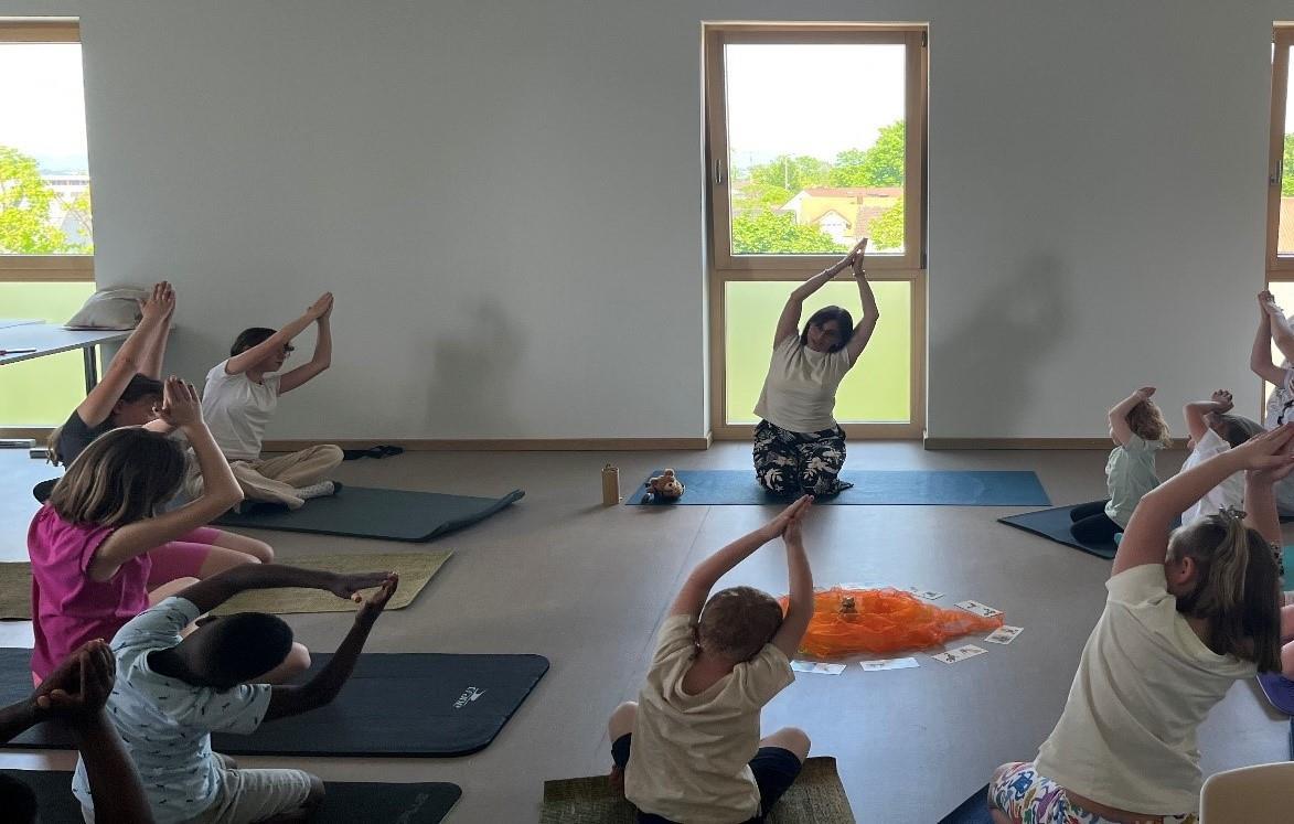 Szene aus der Yogastunde mit Lehrerin und Kindern