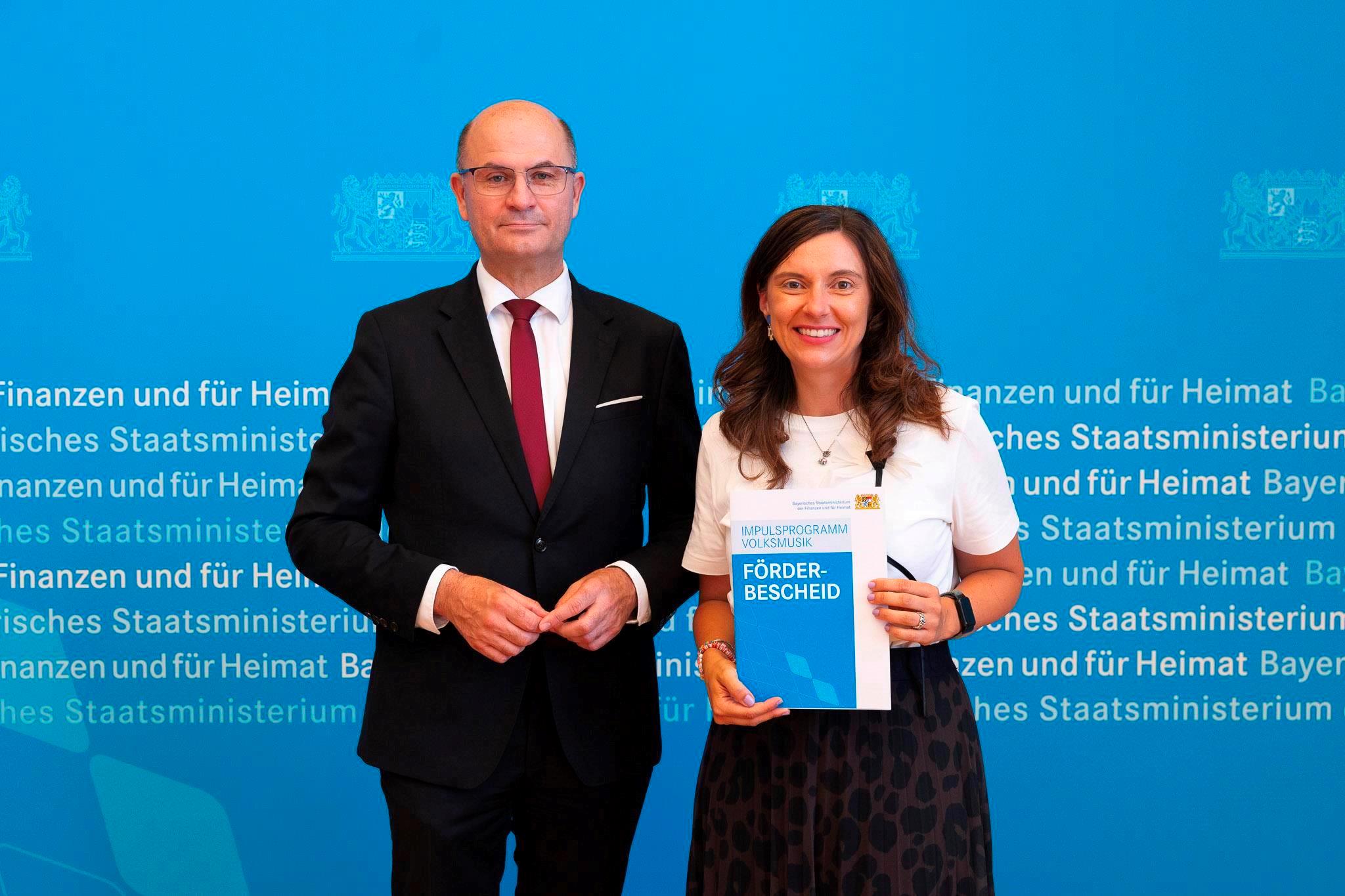 Finanz- und Heimatminister Albert Füracker übergibt Förderbescheid aus dem „Impulsprogramm Volksmusik“ an die Kommunale Jugendpflegerin des Landkreises Straubing-Bogen, Julia Stadler.