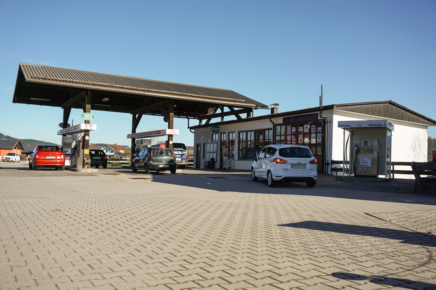 Zu sehen ist die FIT-Tankstelle in Hunderdorf, aufgenommen von der südlichen Einfahrt.
Rechts im Bild ist das Tankstellengebäude mit der Autogas-Zapfsäule.
Insgesamt sind 5 PKWs zu sehen, die gerade tanken bzw. wieder wegfahren.