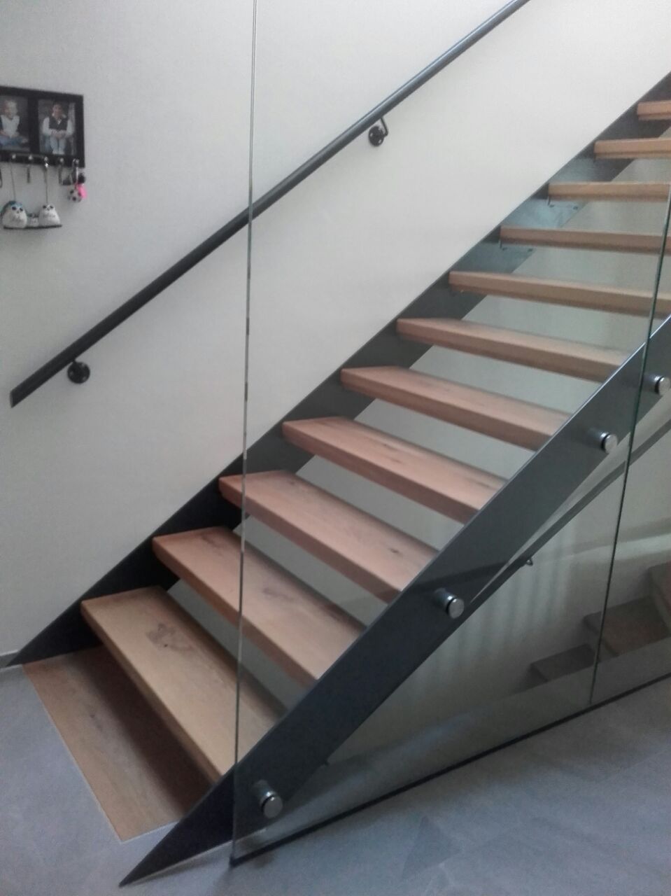 Treppe mit Wangen aus Metall, die Stufen sind aus Holz gefertigt. Rechts als Absturzsicherung deckenhohe Glasscheiben