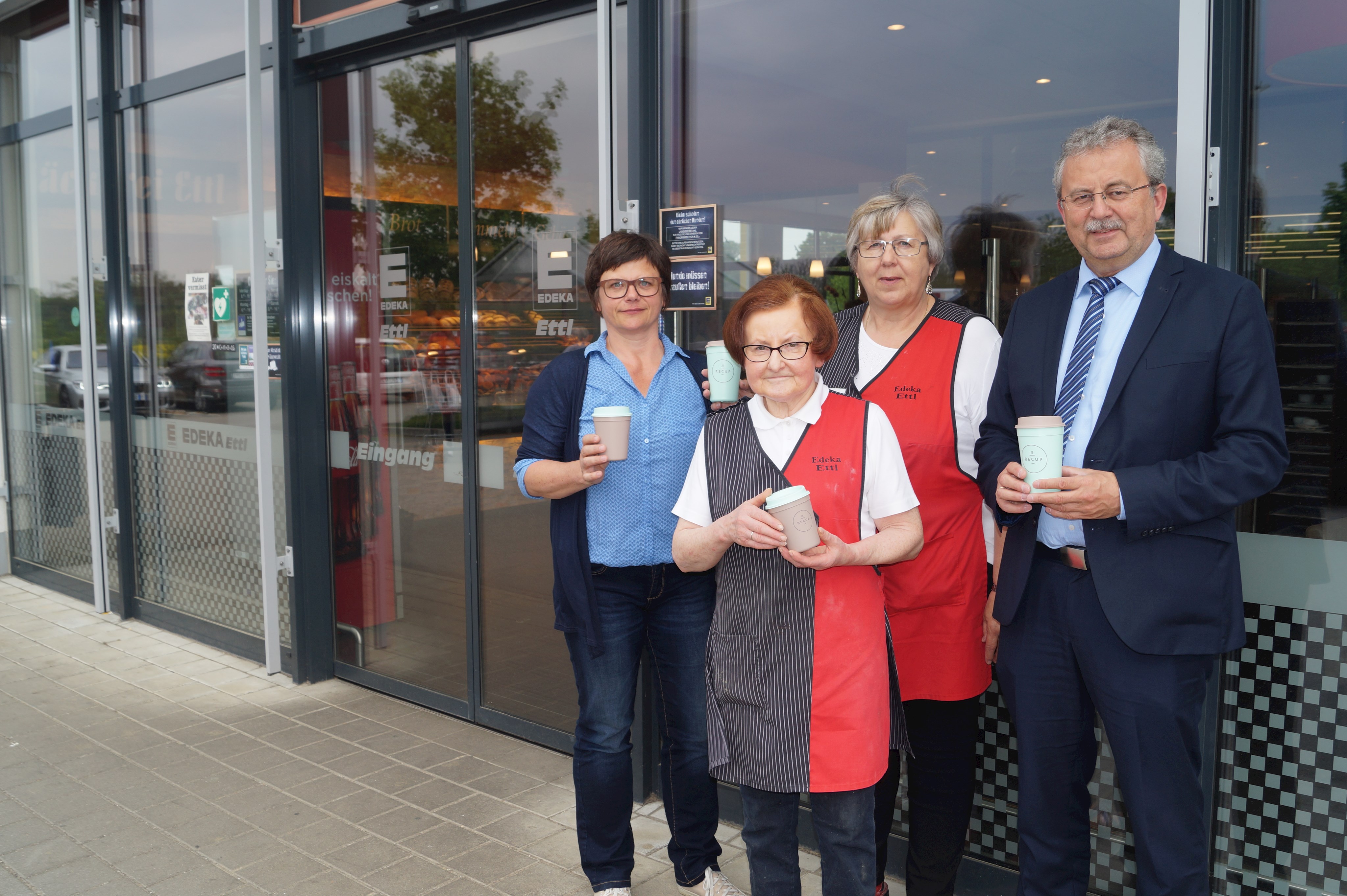 Gudrun Späth (ZAW-SR), Anna Ettl (Inhaberin Edeka Ettl), Angelika Wolf (Marktleiterin Edeka Ettl) und Landrat Josef Laumer (von links) mit den wiederverwertbaren und recyclebaren RECUP-Bechern vor dem Eingang des Edeka-Marktes Ettl in Rain.