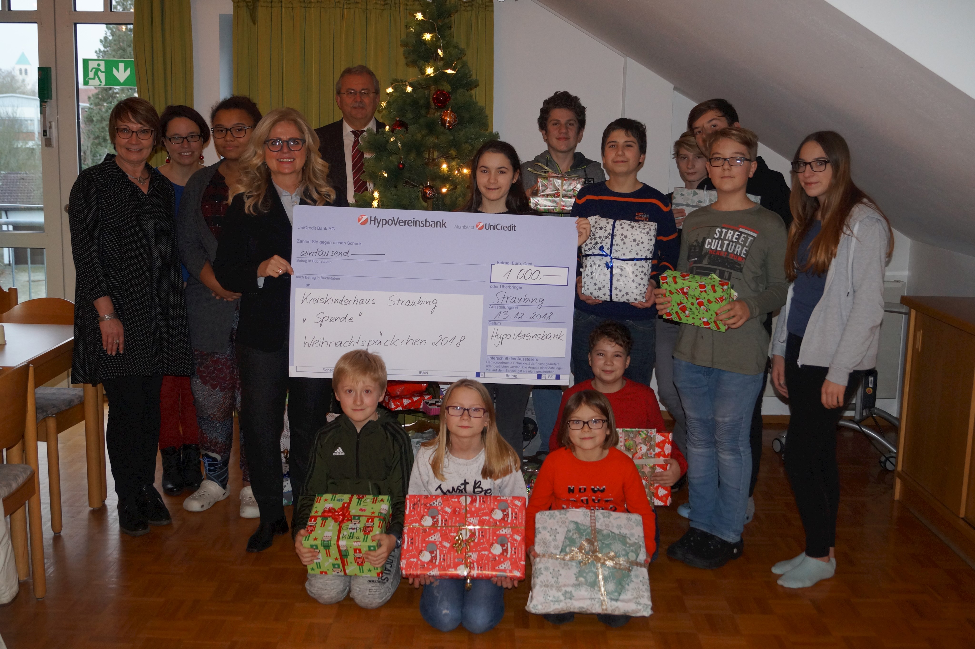 Jutta Robl-Bail (vierte von links), Landrat Josef Laumer und Andrea Semmelmann (ganz links) bei der Scheck- und Geschenkeübergabe mit Kindern aus dem Kreiskinderhaus vor dem Weihnachtsbaum.