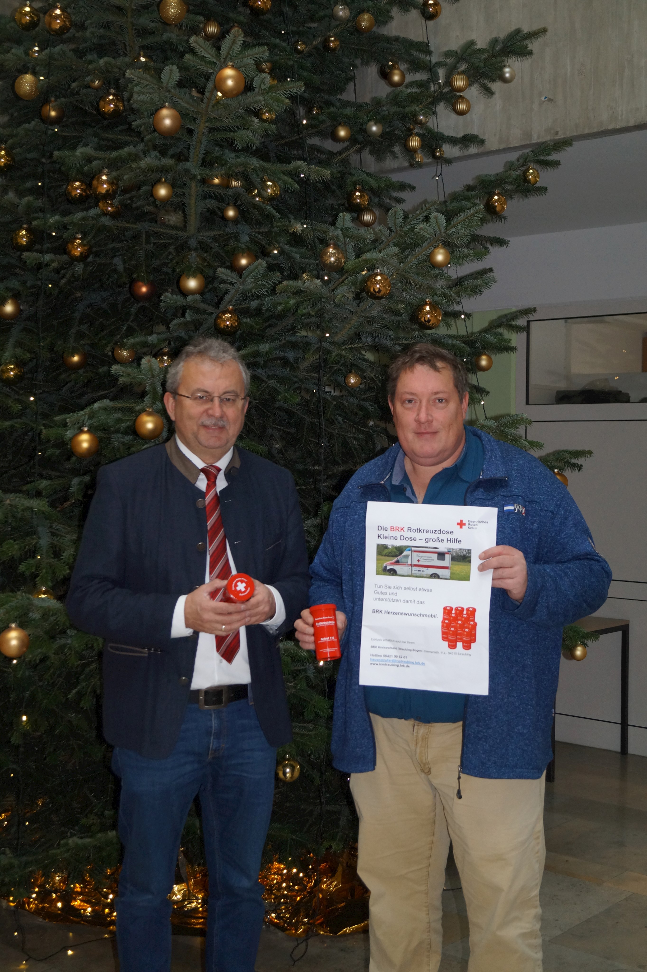 Leider haben wir keinen Titel zu diesem Bild. Wir arbeiten daran und bitten um Ihr Verständnis. Landrat Josef Laumer (links) und der Personalratsvorsitzende Alexander Penzkofer mit der Rotkreuzdose in der Hand vor dem Weihnachtsbaum im Foyer des Landratsamtes.