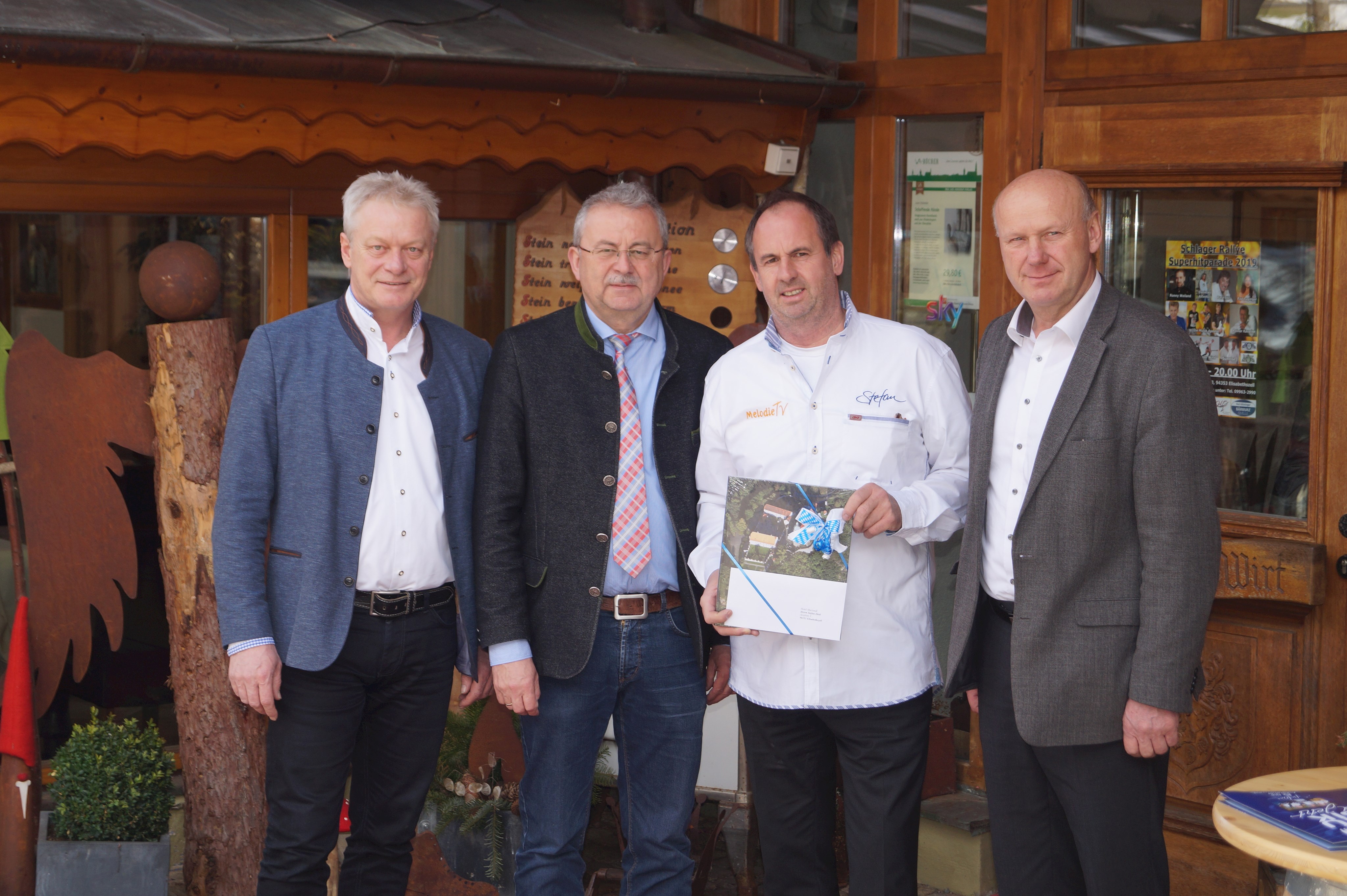 MdB Alois Rainer, Landrat Josef Laumer, Stefan Dietl und Haibachs Bürgermeister Fritz Schötz (von links) vor dem Hotel Mariandl in Elisabethszell. Stefan Dietl hat ein Geschenk des Landkreises in der Hand.