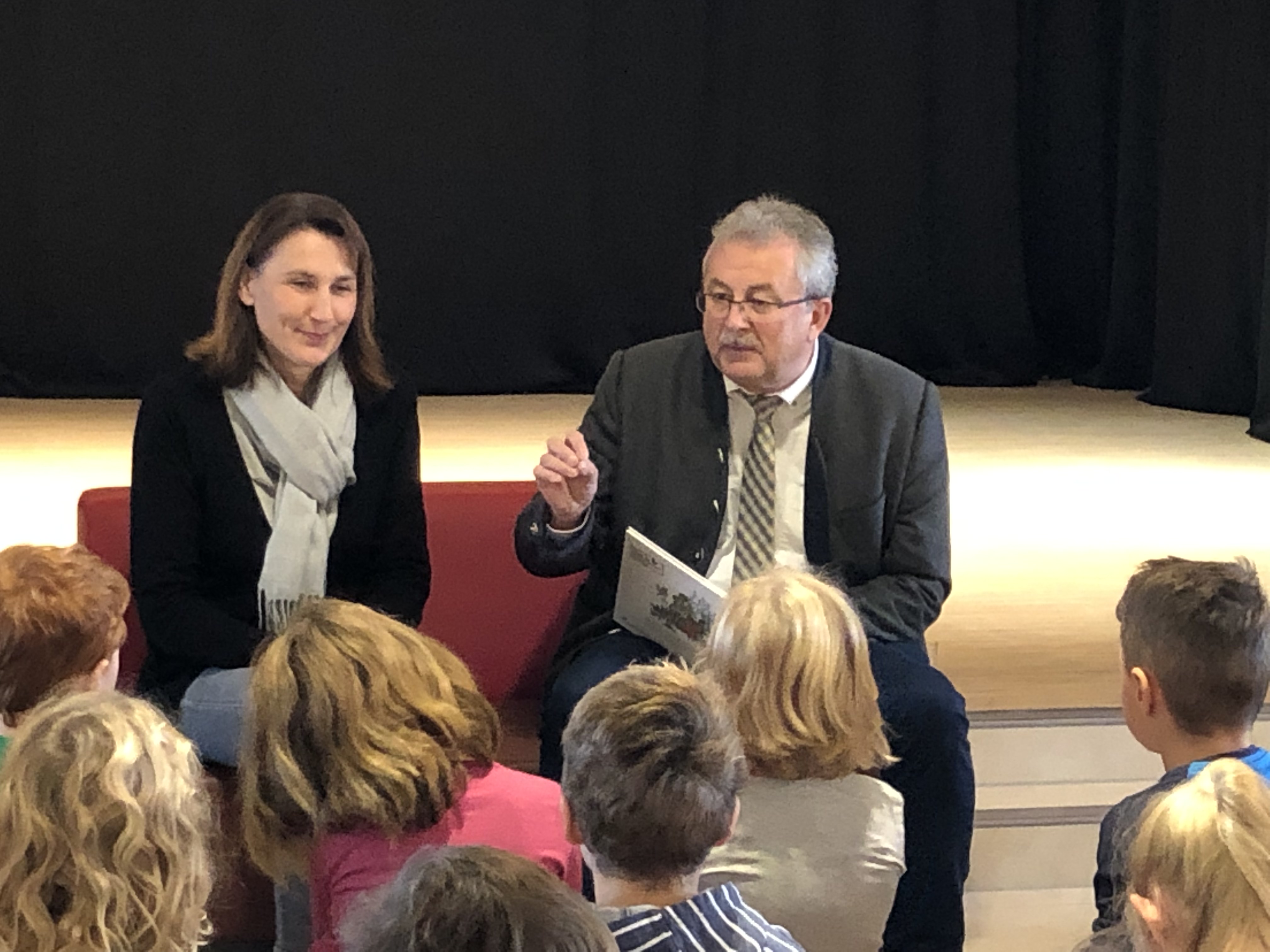 Landrat Josef Laumer beim Vorlesetag in Rain gemeinsam mit Bürgermeisterin Anita Bogner. Das Bild zeigt ihn sitzend beim Vorlesen aus dem Buch.